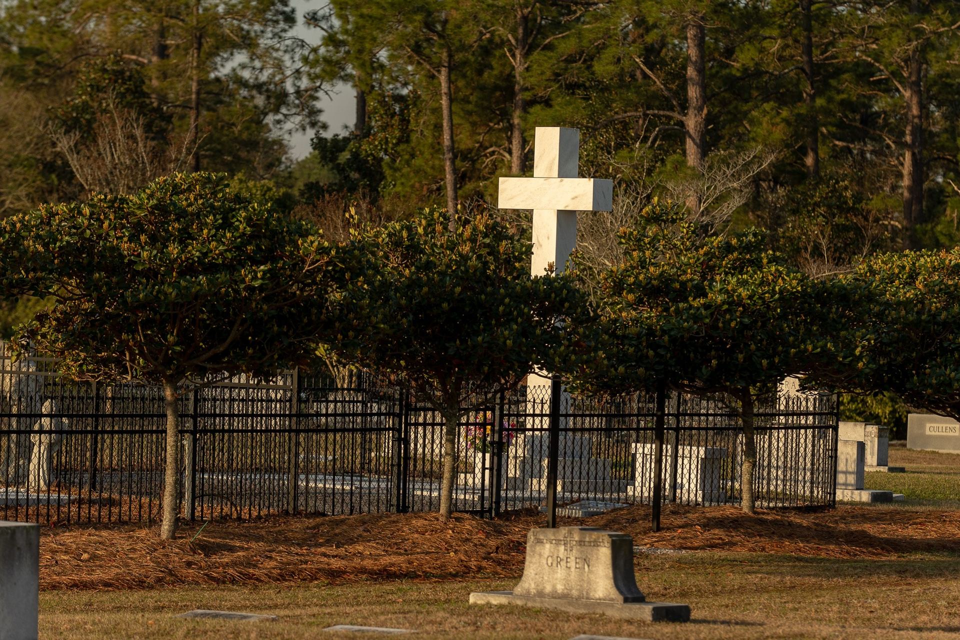 A white cross behind an iron fence at Pine Crest Cemetery